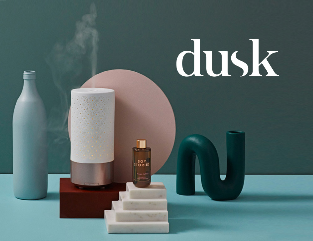 Candles and fragrance products displayed on a teal background, illustrating dusk's new fun and personable brand voice.